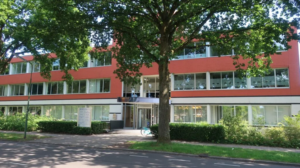 Vooraanzicht van een modern kantoorgebouw aan de Jan van Eycklaan 24, omgeven door groen en schaduwrijke bomen.